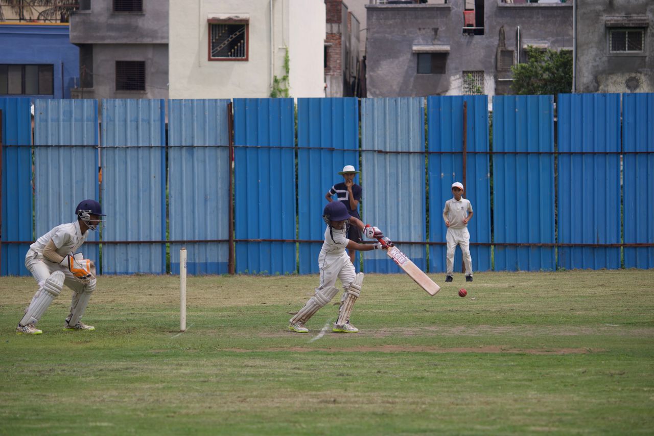 Action shot of teenagers playing cricket on a grassy field in Gahunje, India.
